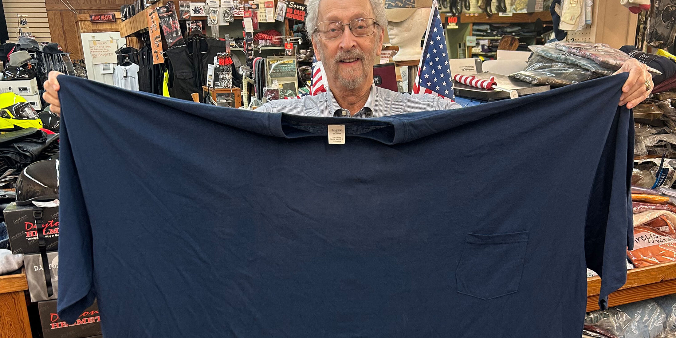 Bubba Kornfeld holding up an oversized navy Big & Tall t-shirt inside Kornfeld's Department Store.