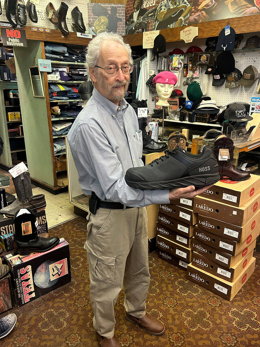 Bubba Kornfeld holding a work shoe beside stacks of Laredo boot boxes.